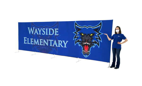 photo of woman wearing a face mask standing next to twenty foot long renovate partition with snarling wolf head graphic and wayside elementary