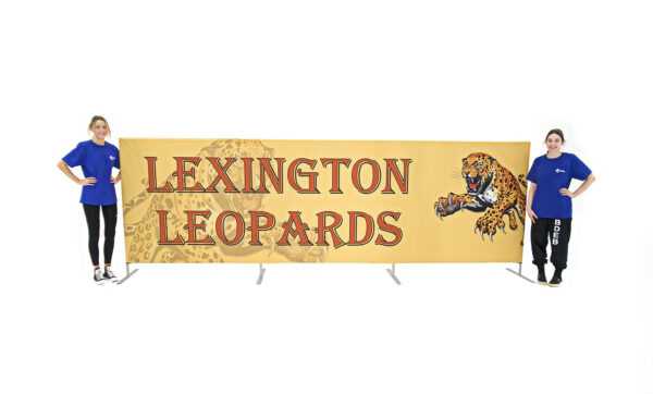 photo of two women standing on either side of a fifteen foot long flow partition with snarling leopard pouncing graphic and Lexington leopards