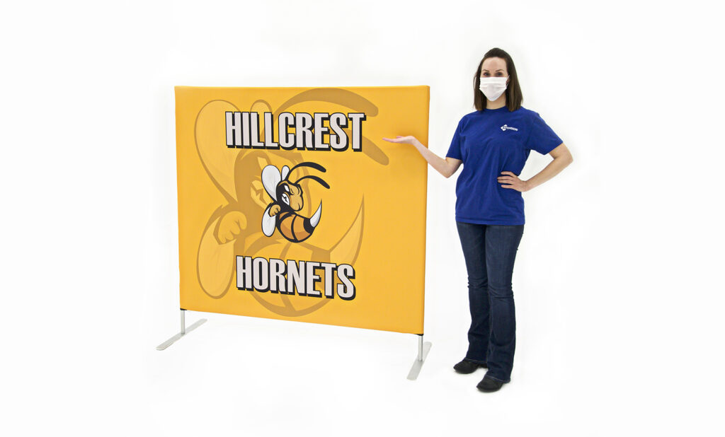 photo of woman in face mask standing next to five foot long flow partition with hornet graphic and hillcrest hornets