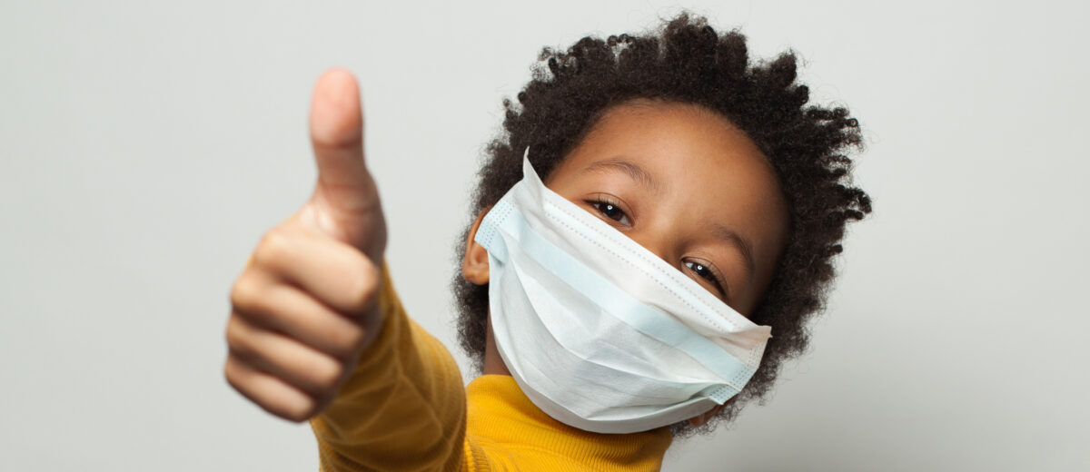 photo of happy African American black kid in medical protective face mask showing thumb up on white